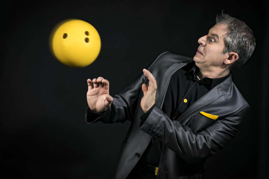 Chris Torrente dans son spectacle de magie Chris de Rire, surpris par l'apparition d'une boule de bowling sur scène lors d'un numéro mêlant humour et magie.